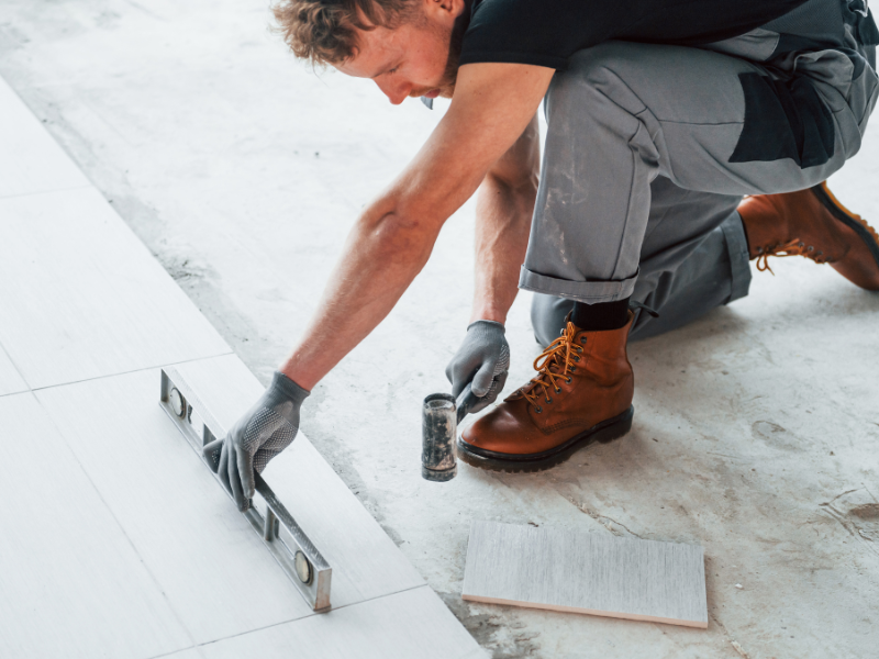 Carreleur installant des carreaux de céramique gris sur le sol d'une salle de bain moderne